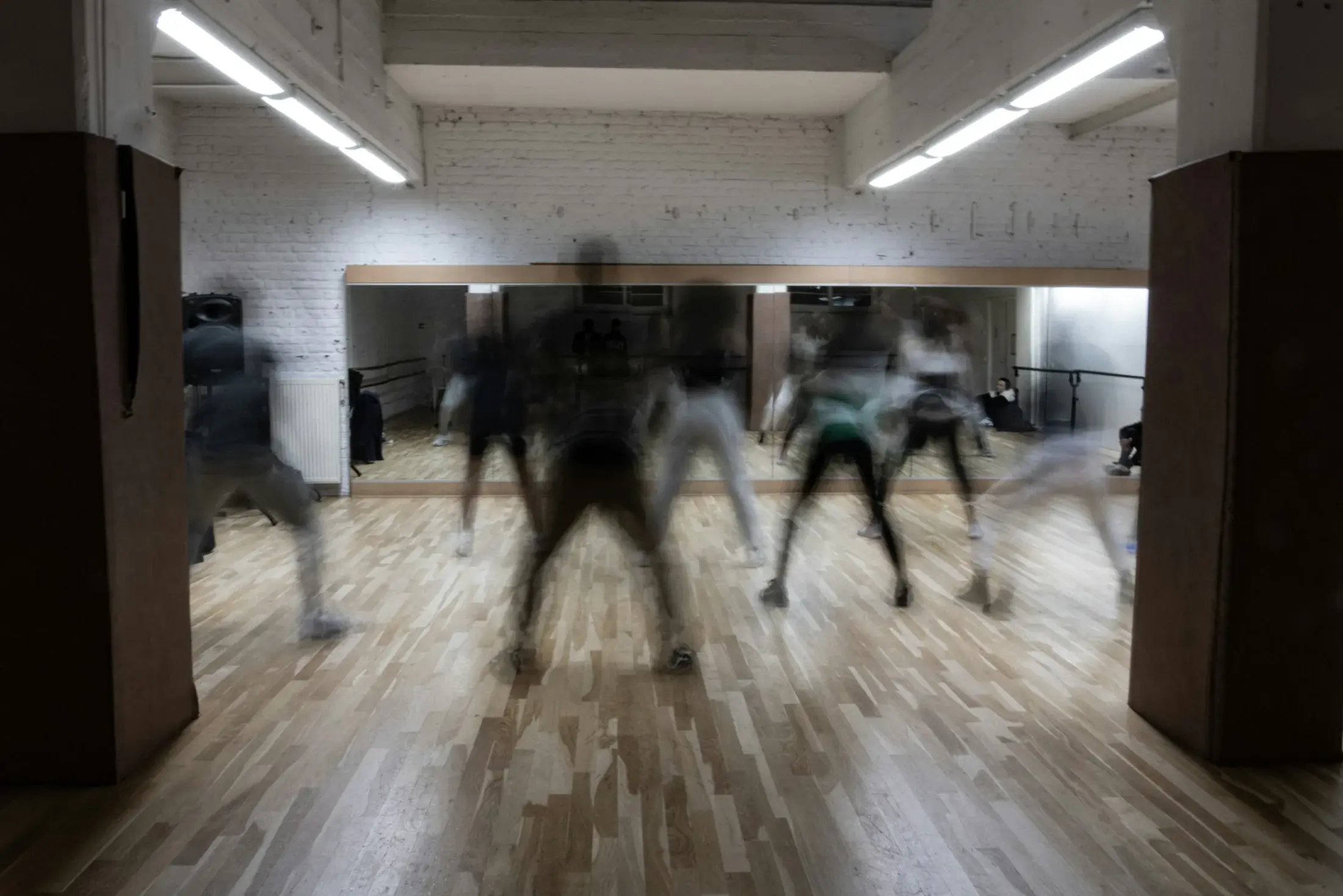 Blurred figures moving across a mirrored studio floor