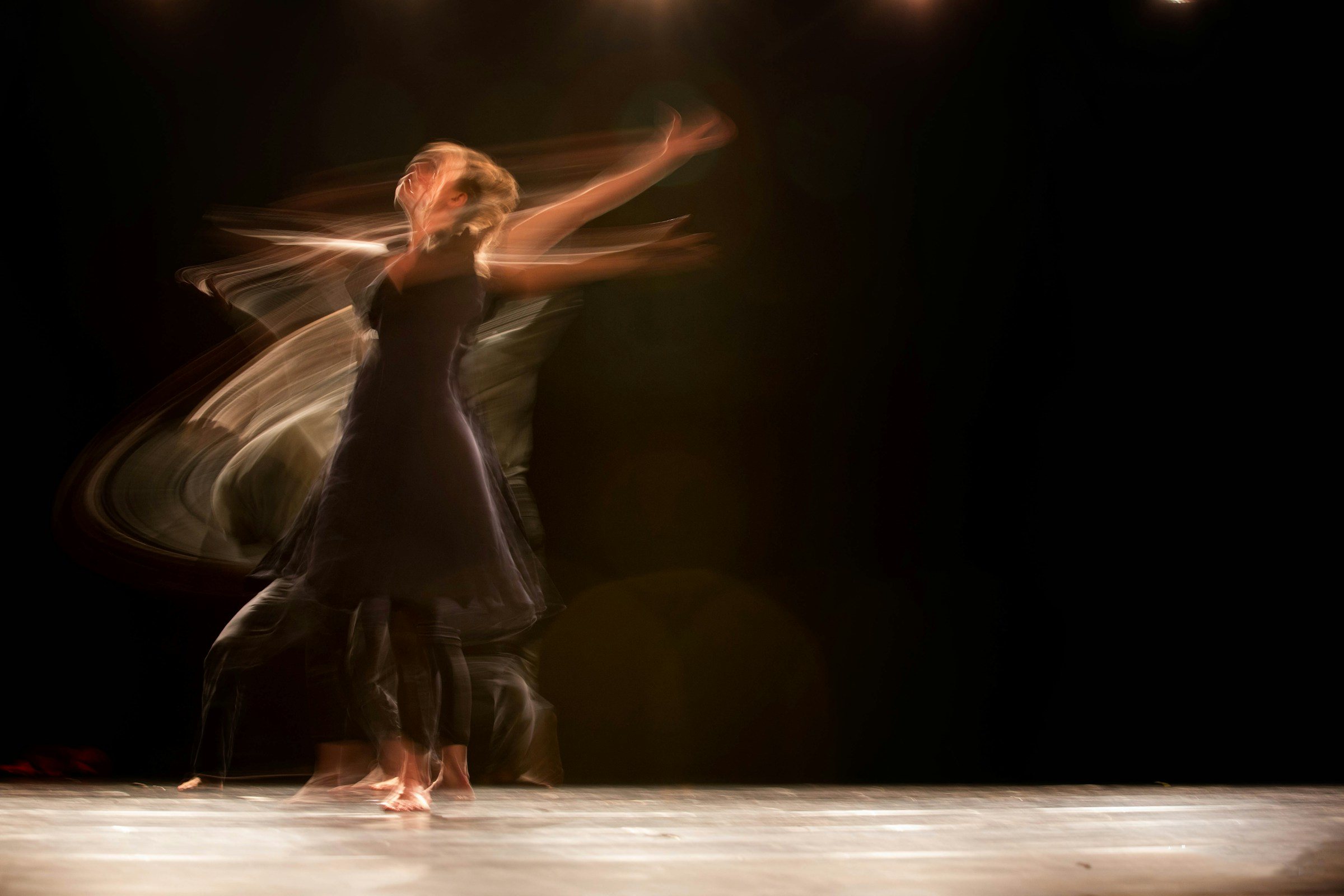 A dancer in a dark dress moving through long-exposure light